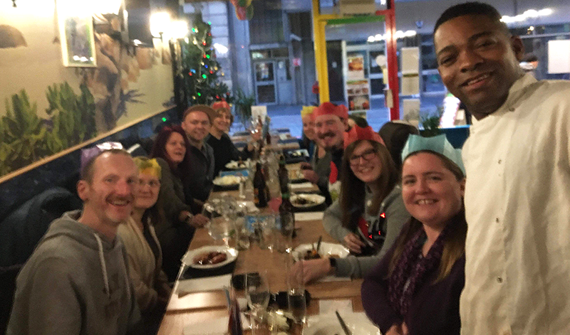 Highland web group members at dining table in Kool Runnings restaurant, all turned towards the camera smiling. Kool Runnings chef is in this picture too.